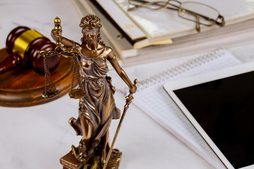 statue of justice with gavel, notebooks, and books in the background