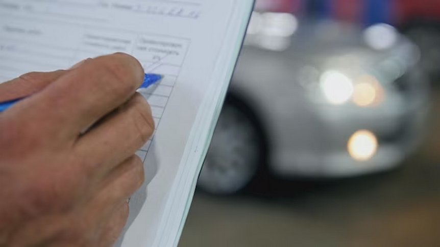 Person writing on a document with a blurred car in the background.