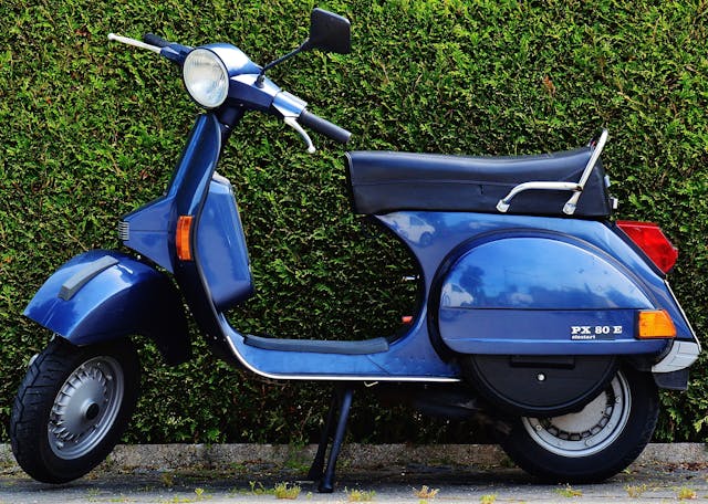 A blue scooter parked in front of a hedge